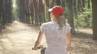 快乐、活泼、活泼的年轻女子在夏日阳光明媚的公园里骑着红帽子`自行车
